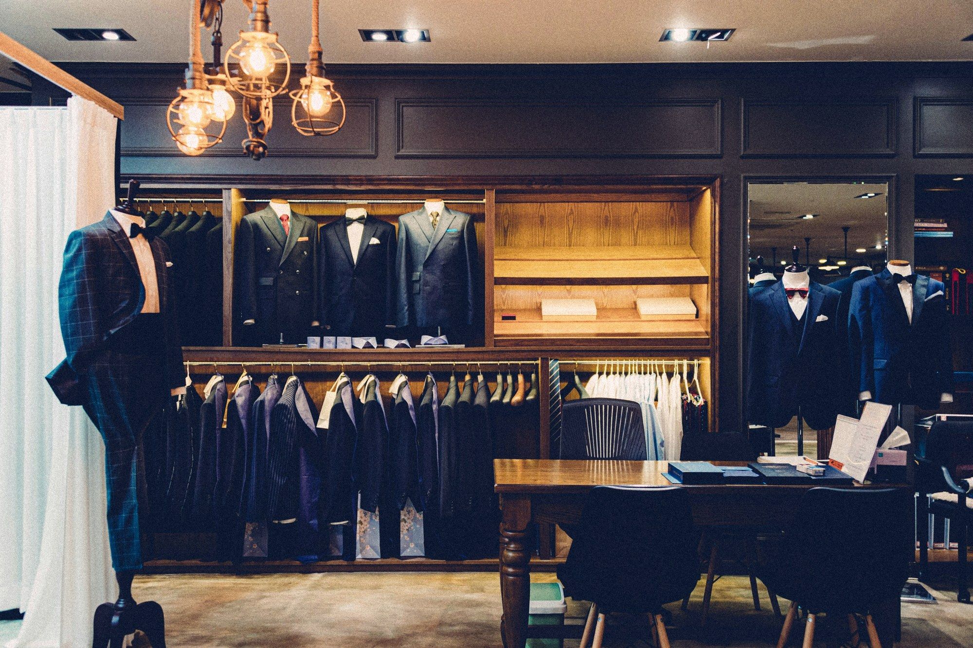 A tailored menswear shop with suits on display under warm pendant lights.